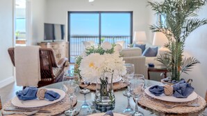 A dining area with a table set for four, a vase with white flowers, and a view of the outdoors through large windows. - Carlos Pointe #532 (Fort Myers Beach)