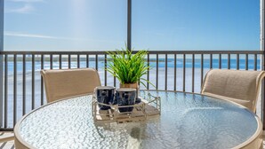 A round glass table with two chairs, a potted plant, and two mugs on a tray. - Carlos Pointe #532 (Fort Myers Beach)