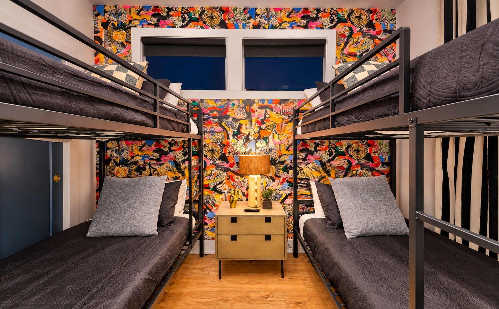 Habitación con literas, un mural colorido, una mesita de noche con lámpara y suelo de madera.