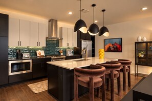A modern kitchen with a central island, stainless steel appliances, and pendant lighting. - Stylish 3BR Nash Escape | Hot Tub + Skyline Views! (Nashville)