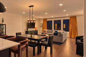 A modern living room with a sofa, a dining area with a table and chairs, and a TV mounted on the wall. - Stylish 3BR Nash Escape | Hot Tub + Skyline Views! (Nashville)