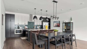 Uma cozinha moderna com armários escuros, uma ilha central e luminárias pendentes.
