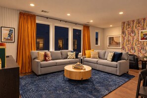 Un salon moderne avec un canapé d’angle gris, une table basse ronde et un tapis bleu.