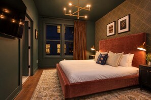 Une chambre à coucher avec un grand lit, une tête de lit, une table de chevet, une lampe et une fenêtre avec des rideaux.