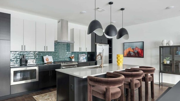 Cozinha moderna com ilha central, eletrodomésticos de aço inoxidável e iluminação pendente.