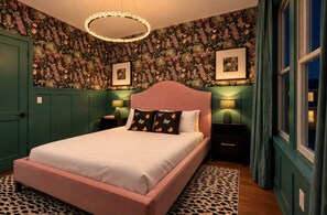 A bedroom with a pink bed, floral wallpaper, two bedside lamps, and a leopard print rug. - Stylish 3BR Nash Escape | Hot Tub + Skyline Views! (Nashville)