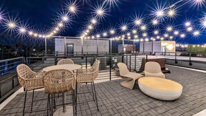 Terraço no telhado com móveis de vime, uma mesa redonda e luzes de festa.