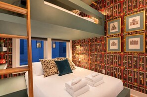 A hotel room with a bed, pillows, a shelf with decorative items, and a wall with framed pictures. - Stunning Lux Nash Home | Rooftop Firepit | 10 Beds (Nashville)