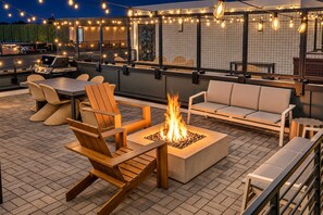 Een terras buiten met een vuurkuil, zitplaatsen en lichtjes.