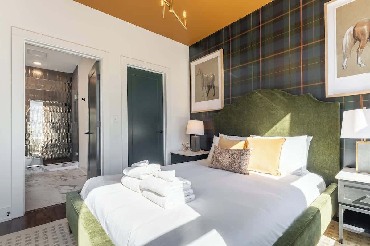 A hotel room with a large bed, a green headboard, a nightstand with a lamp, and a framed picture on the wall.