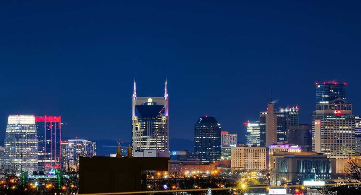 A city skyline at night with illuminated buildings and a prominent tower with two spires.