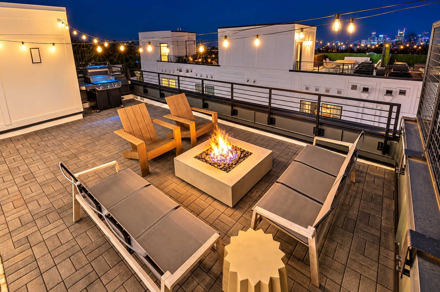 A rooftop terrace with outdoor seating, a fire pit, and city views at night.
