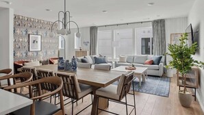 A modern living room with a dining area, featuring a large wooden table, comfortable seating, and a decorative wall. - Designer 3BR Nash Home w/ Private Rooftop Fire Pit (Nashville)