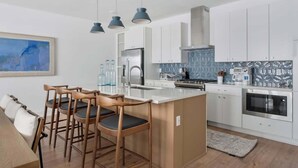 A modern kitchen with white cabinets, a central island with bar stools, stainless steel appliances, and pendant lighting. - Designer 3BR Nash Home w/ Private Rooftop Fire Pit (Nashville)
