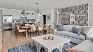 A modern kitchen with white cabinets, a dining area with wooden chairs, and a gray sofa. - Designer 3BR Nash Home w/ Private Rooftop Fire Pit (Nashville)