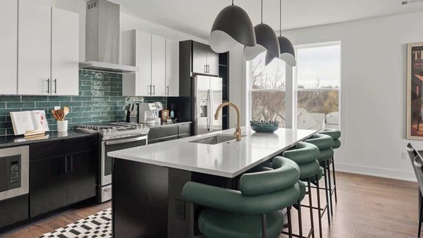 A modern kitchen with a central island, bar stools, and a view of the outdoors.