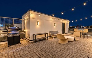 Une terrasse extérieure équipée d’un barbecue, d’un espace salon et de guirlandes lumineuses.