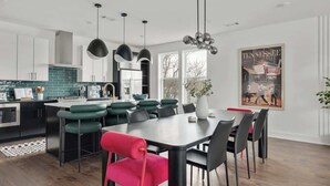 A modern kitchen with a central island, black and green bar stools, a dining table with black chairs, and pendant lighting.