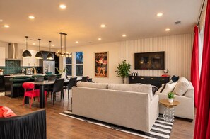Ein modernes Wohnzimmer mit Sofa, Essbereich, Küche und einem an der Wand befestigten Fernseher.