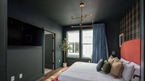 A modern bedroom with a large bed, a dark wall, a window with curtains, and a ceiling light fixture.
