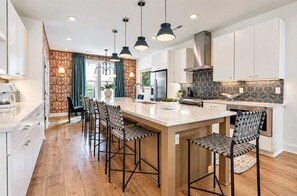 A modern kitchen with a central island, bar stools, pendant lighting, and a backsplash with a geometric pattern. - Upscale 4BR Home w/Rooftop, Hot Tub & Views!7 Beds (Nashville)