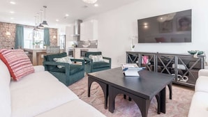 Een moderne woonkamer met een bank, fauteuils, een salontafel en een aan de muur bevestigde televisie.