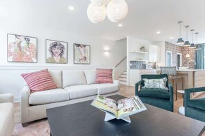 Ein modernes Wohnzimmer mit einer Couch, Sesseln, einem Couchtisch mit einer Zeitschrift und Kunstwerken an der Wand.
