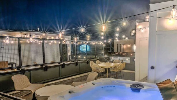 Een dakterras met een jacuzzi, buitenterras, lichtslingers en uitzicht op de stad.
