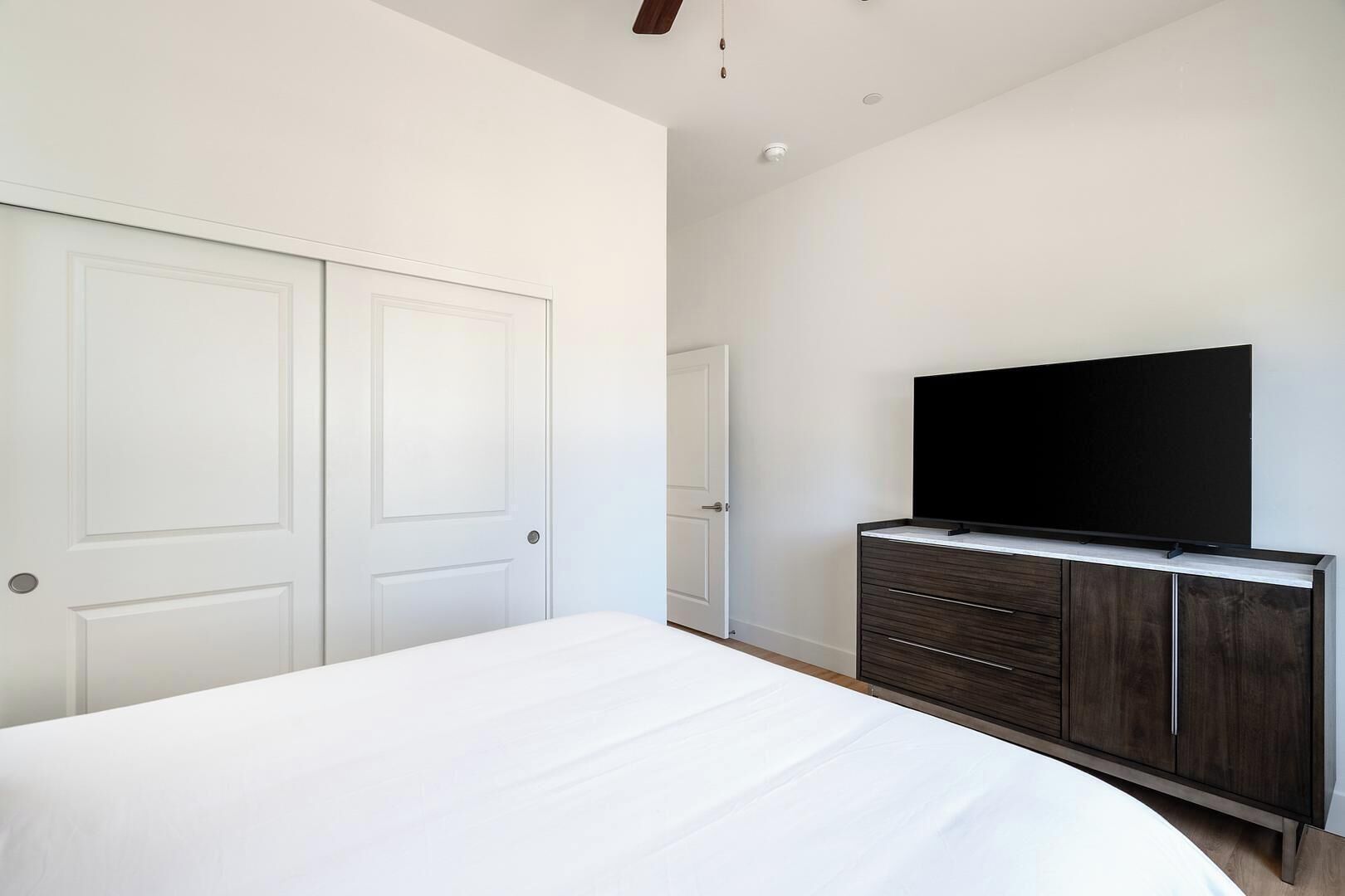 A bedroom with a bed, a dresser, a television, and two doors.