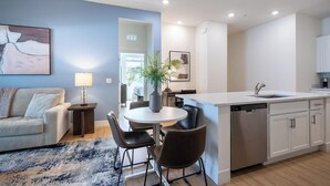 Una cocina moderna con una isla central, un comedor con mesa redonda y sillas, y una sala de estar con sofá y lámpara.