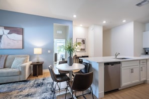 A modern kitchen with a central island, a dining area with a round table and chairs, and a living room with a sofa and a lamp. - Landing | Stunning 3BD, Pool (Casas Adobes)