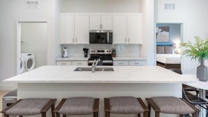 Una cocina moderna con armarios blancos, una isla central con taburetes, un microondas integrado y un lavavajillas.