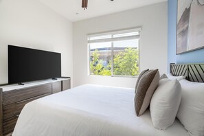 A bedroom with a bed, a TV on a stand, a window with blinds, and a painting on the wall. - Landing | Stunning 3BD, Pool (Casas Adobes)