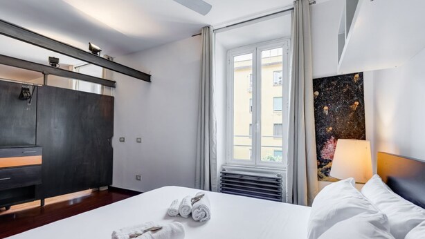 Une chambre d’hôtel avec un lit, un bureau, une chaise, une fenêtre et un tableau au mur.