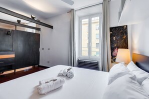 A hotel room with a bed, a desk, a chair, a window, and a painting on the wall. - The Industrial Lab @Piramide (Rome)