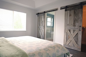 Ein Schlafzimmer mit einem Bett, einem Fenster und einer Schiebetür im Scheunenstil.