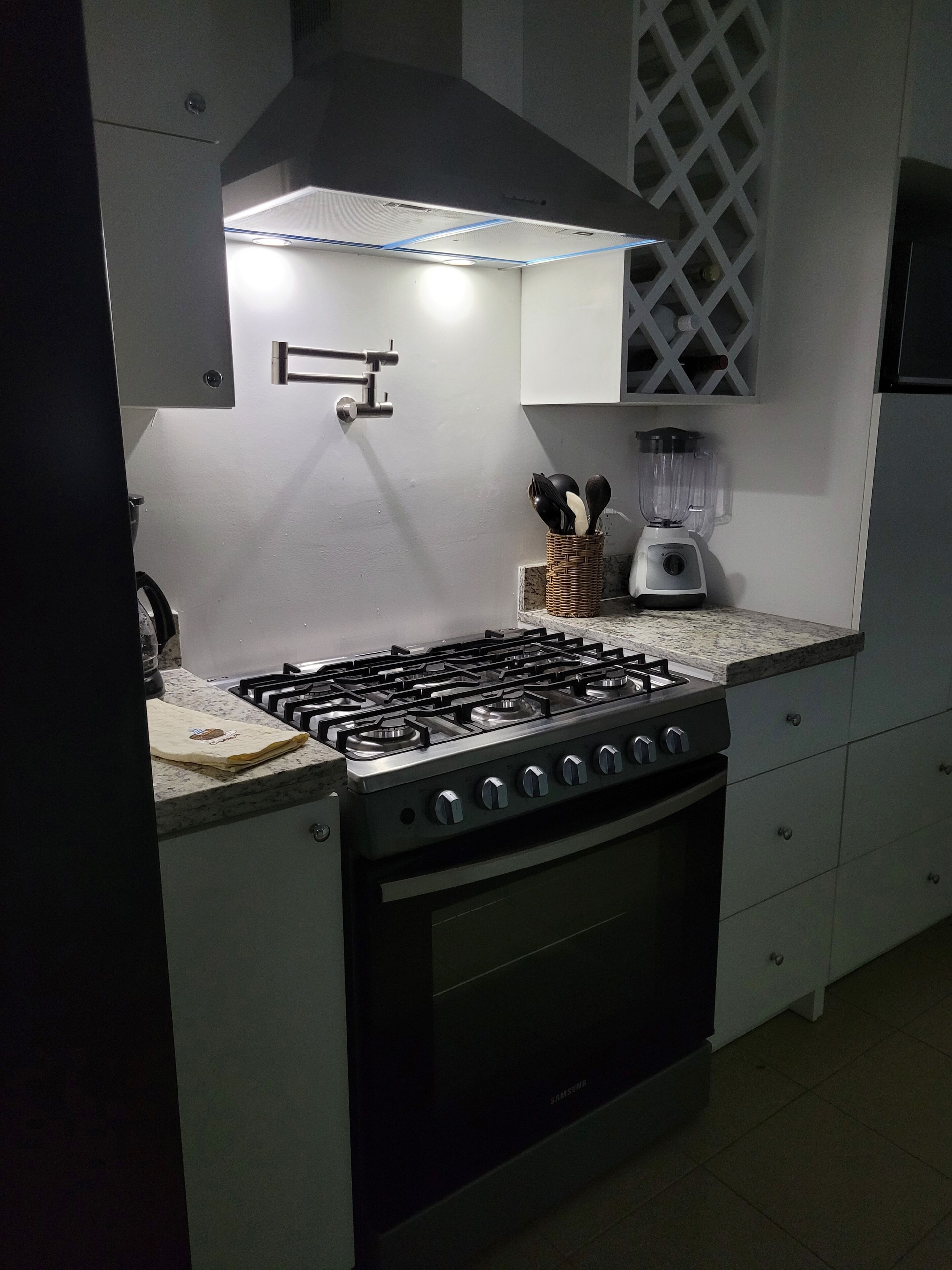 A kitchen with a gas stove, a built-in oven, a blender, and a white cabinet.