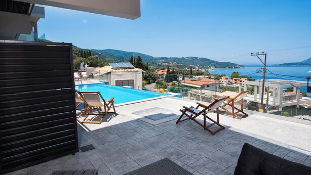 Une terrasse sur le toit avec une piscine, des chaises longues et une vue sur la mer et les collines.
