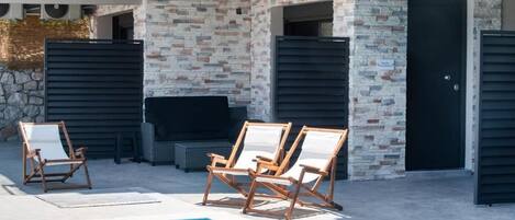 A modern outdoor pool area with a stone wall, two lounge chairs, and a built-in entertainment unit.
