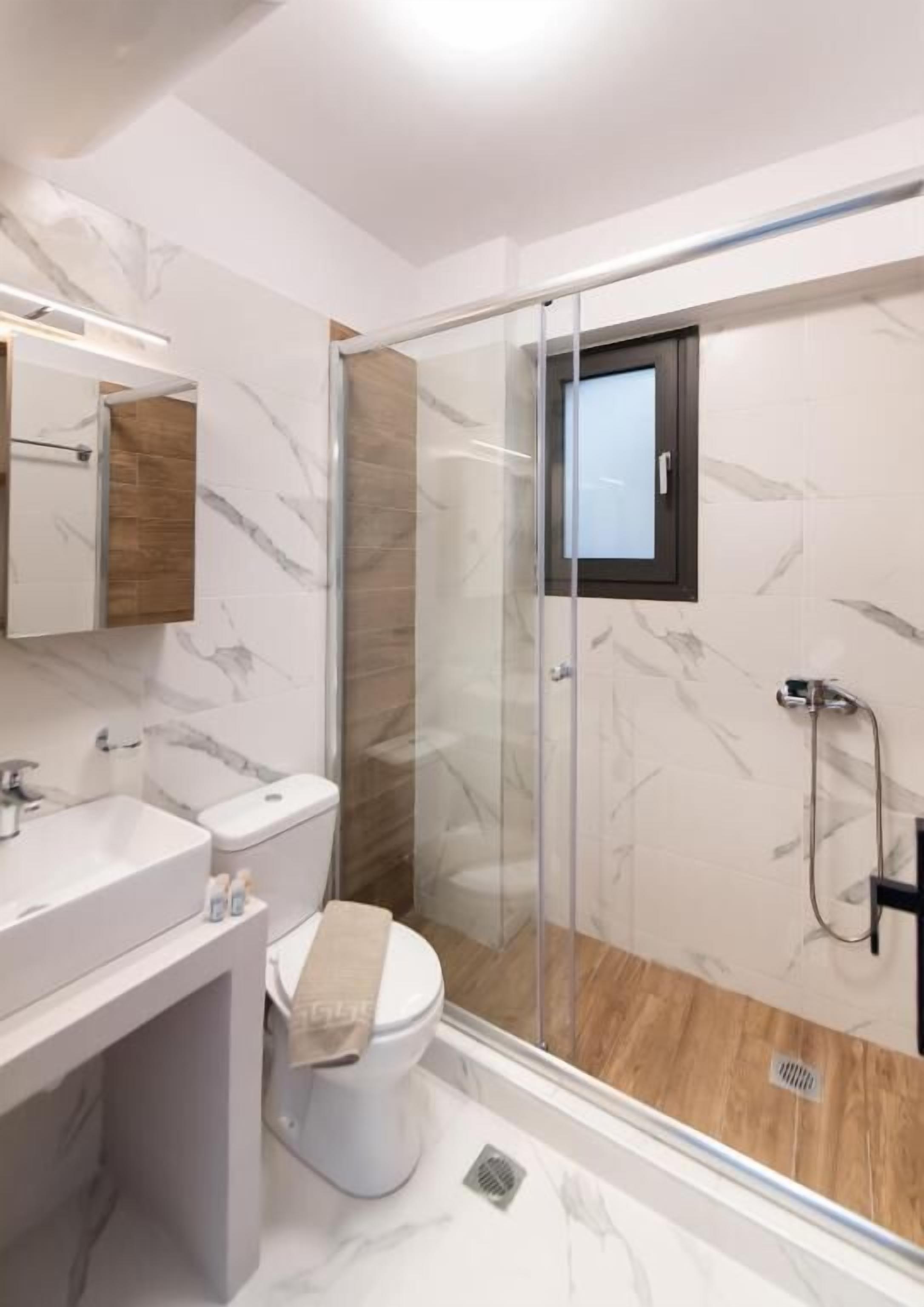 A modern bathroom with a glass-enclosed shower, a white toilet, and a marble-tiled vanity.