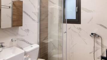 A modern bathroom with a glass-enclosed shower, a white toilet, and a marble-tiled vanity.