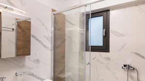 Une salle de bain moderne avec une douche à parois de verre, des carreaux de marbre, un meuble-lavabo en bois et des toilettes blanches.