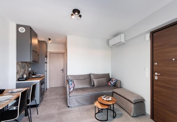 A compact living space with a kitchenette, a sofa, a small table, and a bench. - Amaryllis Luxury Apartment (Nikiana)