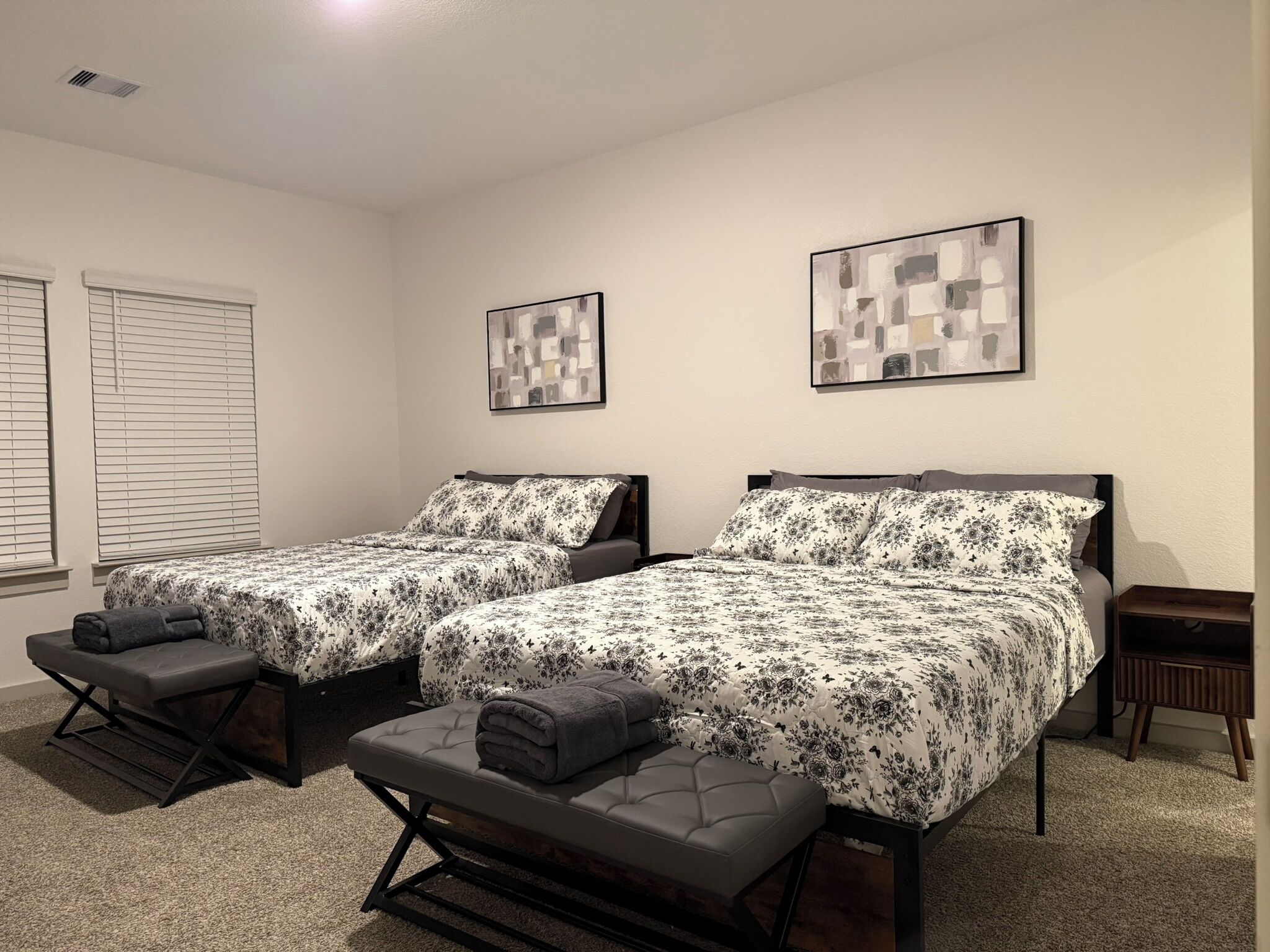 A room with two beds, each with a matching pillow and a bench. There are two framed pictures on the walls.