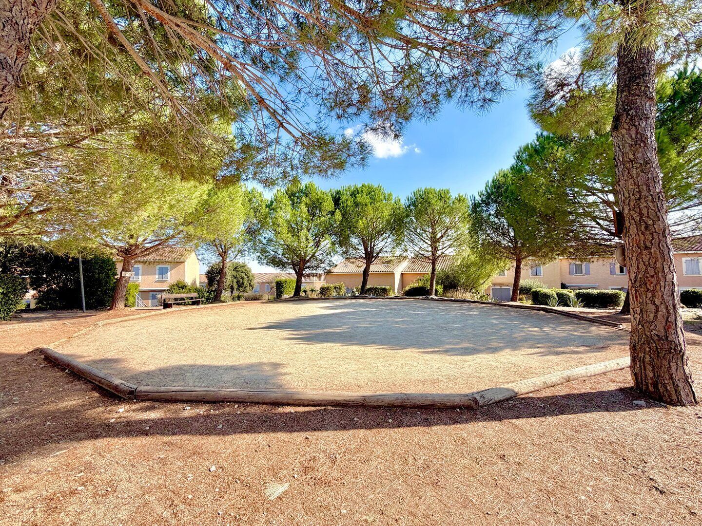 Un patio con suelo de grava, rodeado de árboles y edificios residenciales.