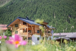 Eine Holzhütte mit Balkon, vor einer bewaldeten Berglandschaft.