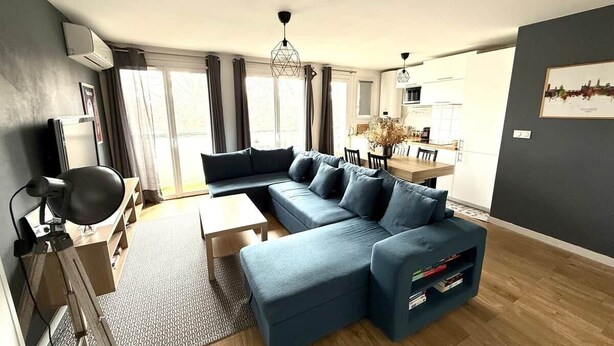 A modern living room with a sectional sofa, a dining area, and a kitchen in the background. - L'Ecrin St Aubin (Toulouse)
