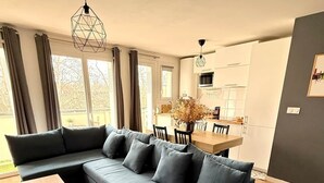 A modern living room with a sectional sofa, a dining table, and a kitchen in the background. - L'Ecrin St Aubin (Toulouse)