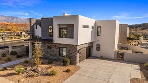 Une maison moderne à deux étages, dotée d’un toit plat, de grandes fenêtres et d’une allée pavée.