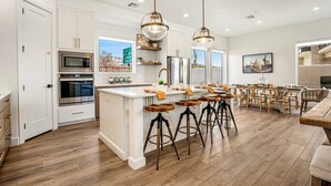 A spacious kitchen with a central island, bar stools, and a dining area with wooden chairs.
